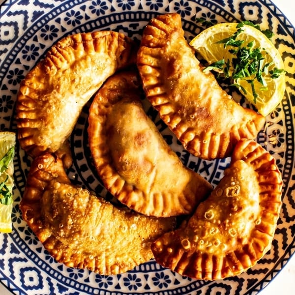 Golden-brown empanadas with lemon wedges and parsley on a blue and white patterned plate.